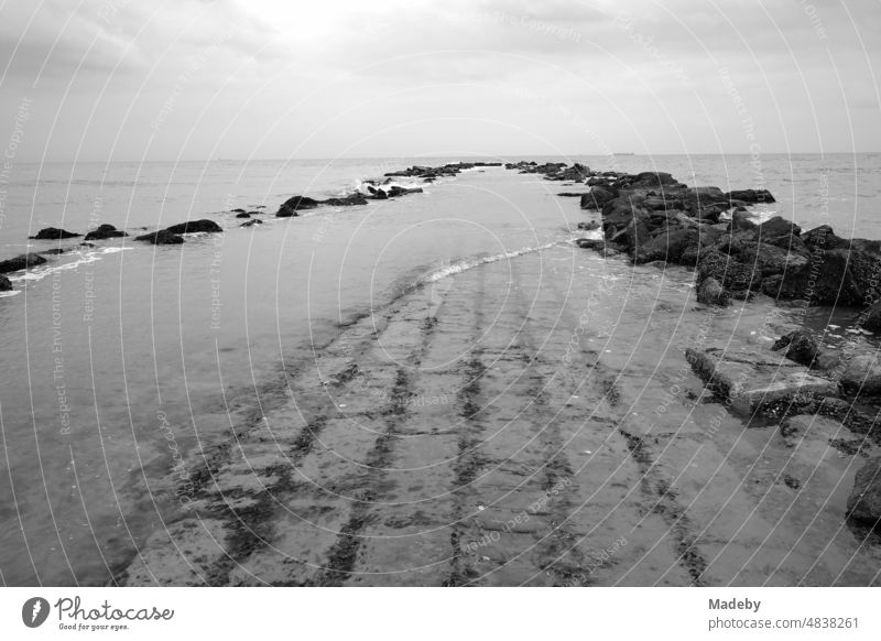 Stones and masonry as breakwaters for coastal protection in rainy weather on the beach in Knokke-Heist on the North Sea near Bruges in West Flanders in Belgium, photographed in classical black and white