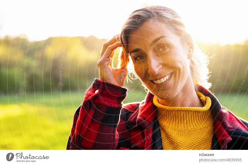 Portrait of beautiful mature woman smiling and looking away at park during sunset. Outdoor portrait of a smiling girl. Happy cheerful girl laughing at park with checkered shirt.