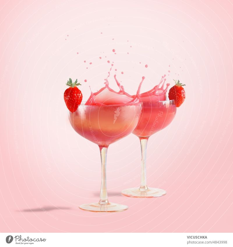 Pink cocktail splashing in champagne glasses with strawberries at pink background with sunlight. Liquid in motion. liquid in motion fancy drinks front view