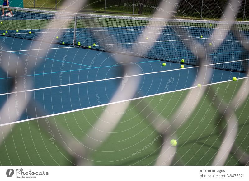 tennis court through blurry diamond shaped fence with balls on the court a person's legs in the distance activity chain chain link fence exercise game gate