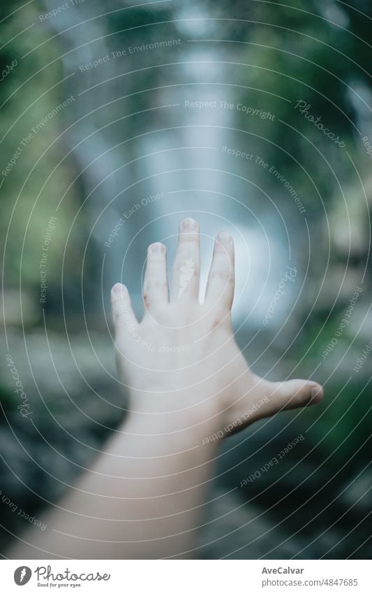 Moody image of an selective in focus hand in front of a waterfall during a sunny day, peaceful scenario, copy space. help and self help concept, mental health concept. Therapy and looking for help