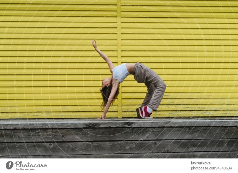 Young female in white top and linen pants dancing in front of yellow wall woman dancer outdoors choreographer girl stylish urban movement sport workout outside