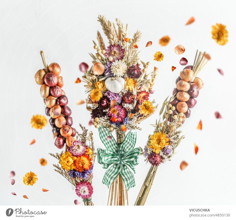 Onion and garlic braids with dried flowers and flying petals at white background. onion rustic autumn setting vegetables front view natural red blossom