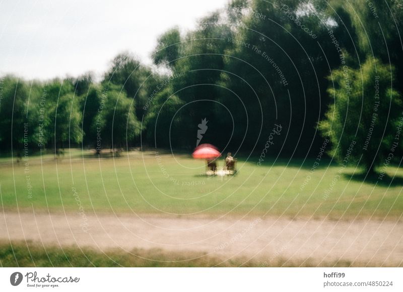 blurred view of two people sitting on chairs with umbrella in park hazy vibrating ICM technology two persons couple Park Relaxation Sunshade pink umbrella Pink