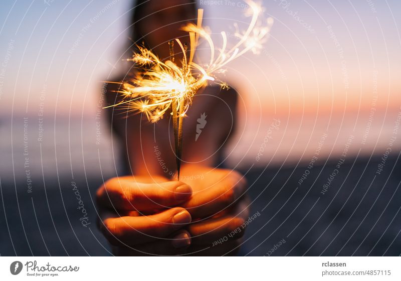 Young happy woman stands on beach with sparkler in sunset light firework holding night girl party people summer abstract background burning celebration flame