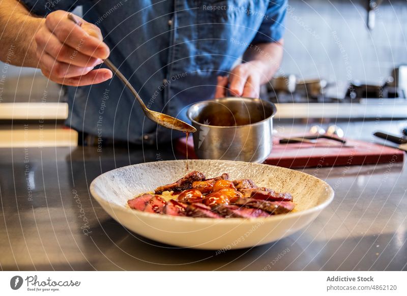 Anonymous Chef Pouring Sauce On Beef In Bowl At Restaurant Commercial Kitchen Spoon Dish Preparing Finishing Dressing Gourmet Garnish Cuisine Steak Counter