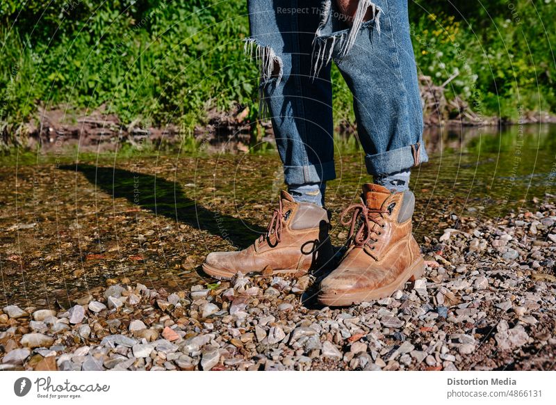 Feet of a hiker wearing boots on the bank of a river, ready to continue his journey active activity adventure autumn backpacker climbing closeup extreme feet