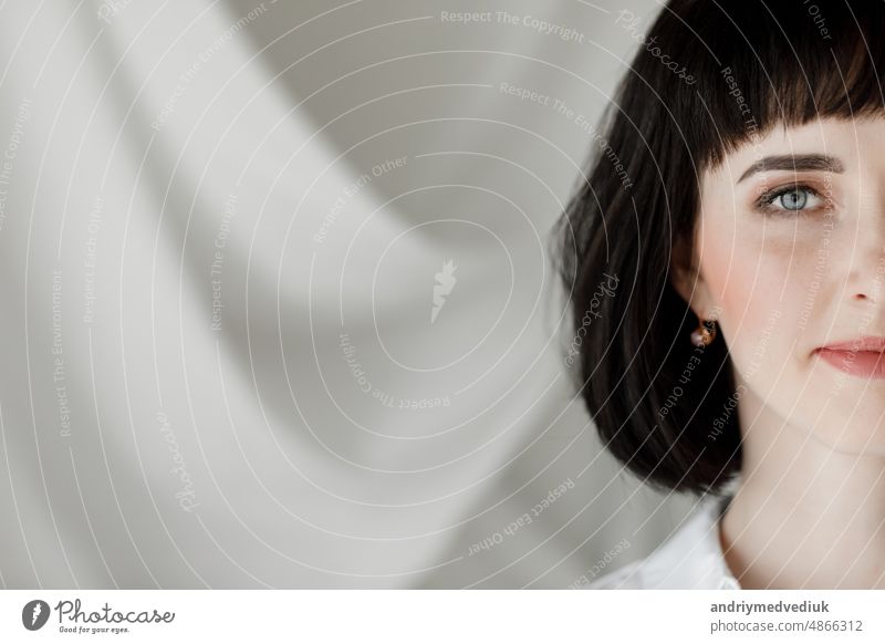 portrait of beautiful brunette young woman with short hair is looking at the camera against the background of a wall with white cloth. copy space. leather skirt