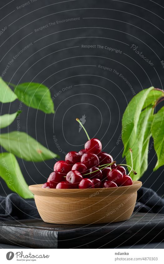 Ripe red cherries in a wooden plate on a black table cherry nutrition berry closeup dessert food fresh freshness fruit green group healthy ingredient juicy leaf