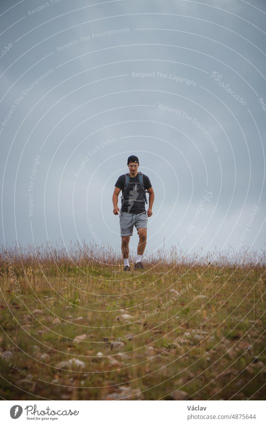 Swarthier type of man is running down a gravel hill, checking his every step to avoid injury. Active athlete runs over challenging terrain to improve fitness, coordination and precision of movement