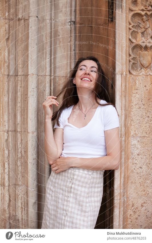 Young female tourist posing near old cathedral. Neutral colors in clothes style. Beige color walls. Woman tourist wearing white t-shirt. summer tourism woman