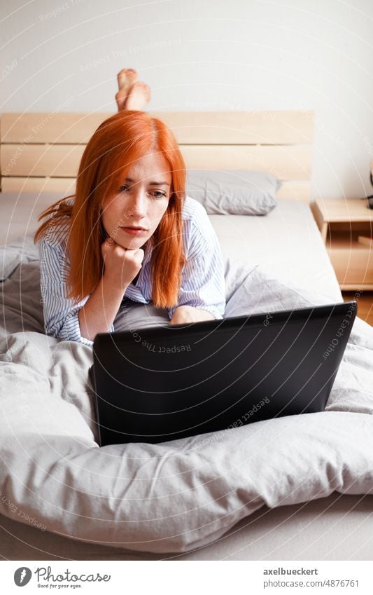 young woman lying on bed with laptop computer watching streaming bedroom home entertainment real people communication bored relax work from home home office