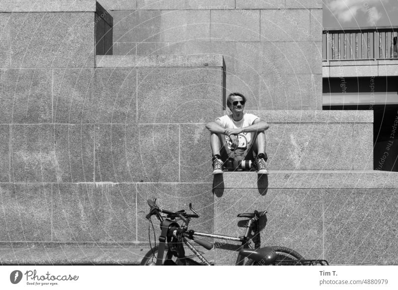a man sits on a step under him a bicycle Man Wheel Bicycle Berlin Middle city palace b/w bnw Day Black & white photo Exterior shot Capital city Downtown