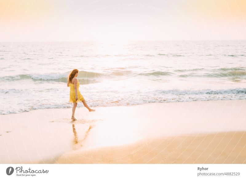 Goa, India. Young Caucasian Woman In Yellow Dress Walking Along Seashore In Summer Sunlight Arabian Sea Indian Ocean beautiful caucasian copy space distance