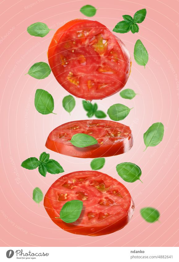 Round red slices of tomato and basil leaves levitate on a pink background. vegetable food leaf spice fall green vegetarian diet ingredient organic healthy cut