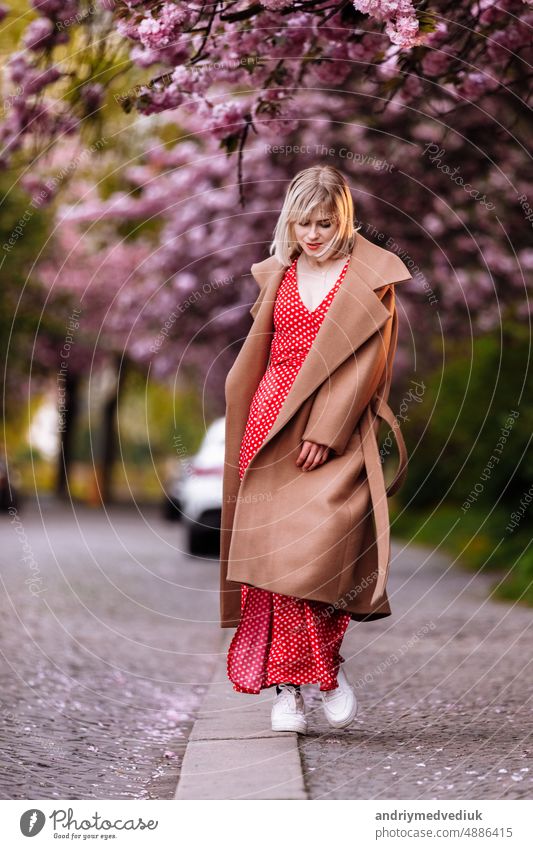 stylish blonde in a red dress in the spring city. Beautiful girl in red dress posing on city streets. Stunning young woman walking in the city. beautiful pretty