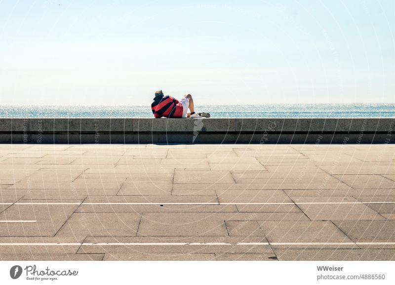 A middle-aged man lies on a wall in the sun and looks at the sea Ocean coast ocean Wall (barrier) Promenade Street pavement Lie rest relaxed Man person