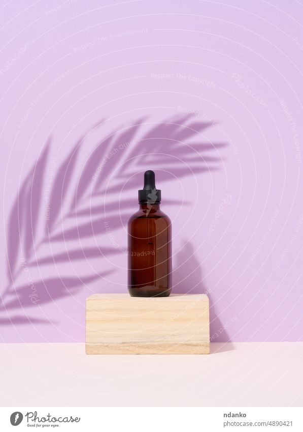 Brown glass bottle with a pipette on purple background. Palm leaf shadow body care podium cosmetic dropper skin care palm product wellness wooden aroma