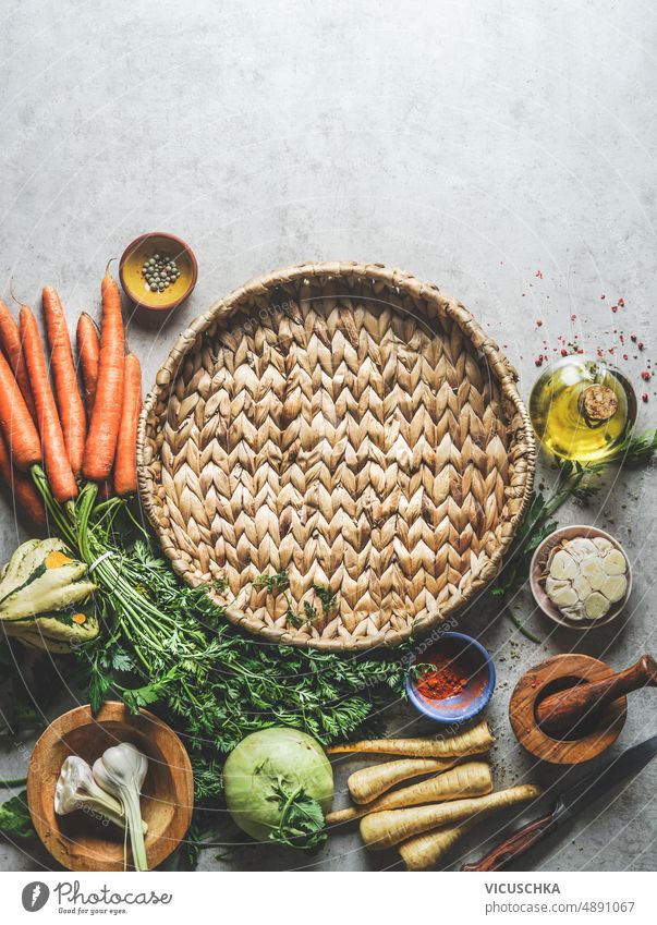 Healthy food background with round tray with various vegetables, oil, herbs and spices at grey concrete kitchen table healthy frame tasty vegetarian cooking