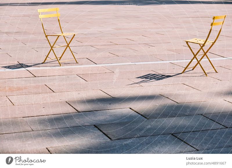 two empty yellow folding chairs face each other in a public place and cast long shadows Places Yellow Empty Sun sunny Shadow Appealing Town urban Folding chairs