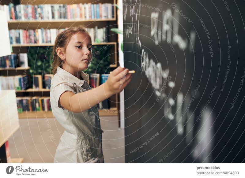 Little girl writing on blackboard. Smart student put solve on chalkboard. Back to school. Child having class. Schoolgirl learning at primary school back child