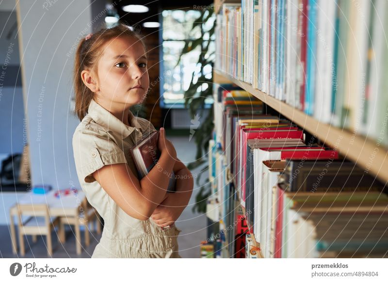 School girl looking at bookshelf in school library. Smart girl selecting literature for reading. Books on shelves in bookstore. Learning from books. Back to school. School education