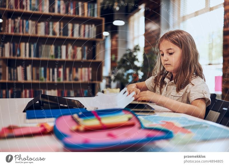 Schoolgirl learning, playing, doing puzzles and reading book in school library. Primary school pupil is engaged in book with jigsaw. Child curiosity back