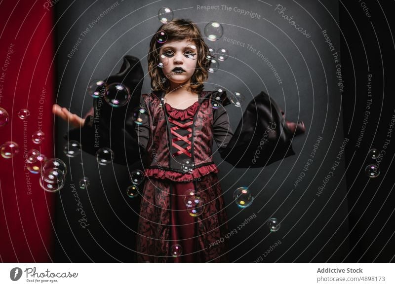 Serious little kid with black lips catching soap bubbles during carnival child halloween costume serious dark magic enchantress portrait girl spooky party