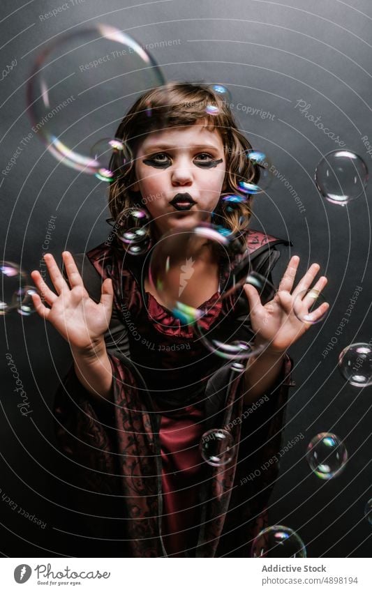 Cute little girl in gothic style outfit with soap bubbles in studio halloween witch celebrate pouting lips kid costume portrait witchcraft carnival childhood