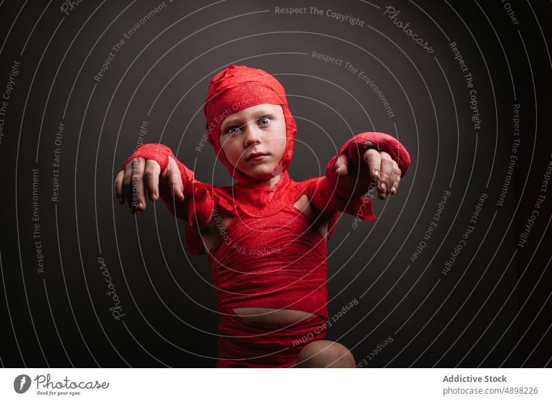 Cute little kid in mummy costume shouting and gesturing in grey studio child halloween boy scary portrait spooky reach out make face creepy adorable celebrate