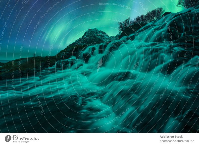 Fast waterfall flowing through rocks under bright Northern Lights aurora borealis environment night cliff river glow nature polar northen lights