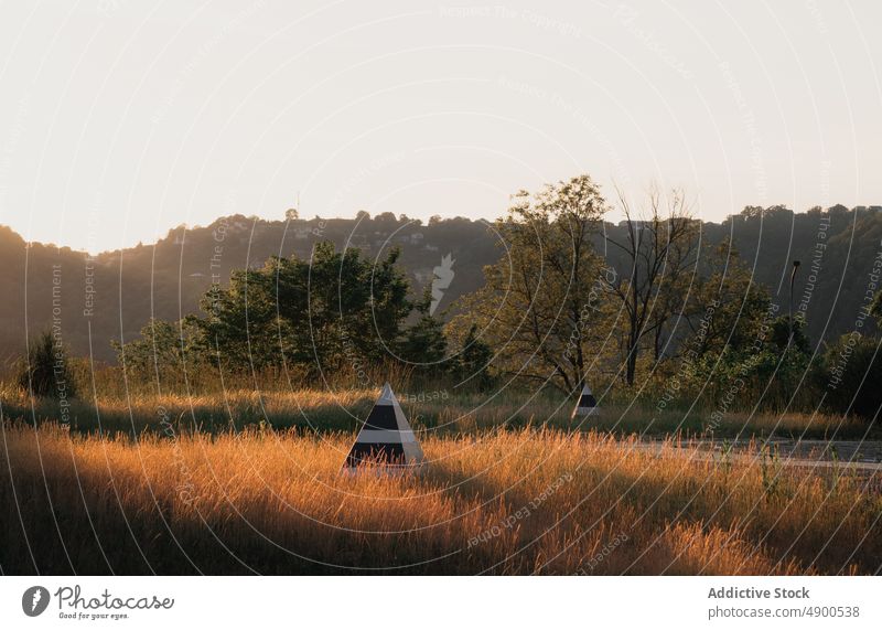 Striped pyramids in countryside at sunset autumn evening grass bush tree sunlit season weather flora shrub foliage vegetate landscape nature dusk twilight fall