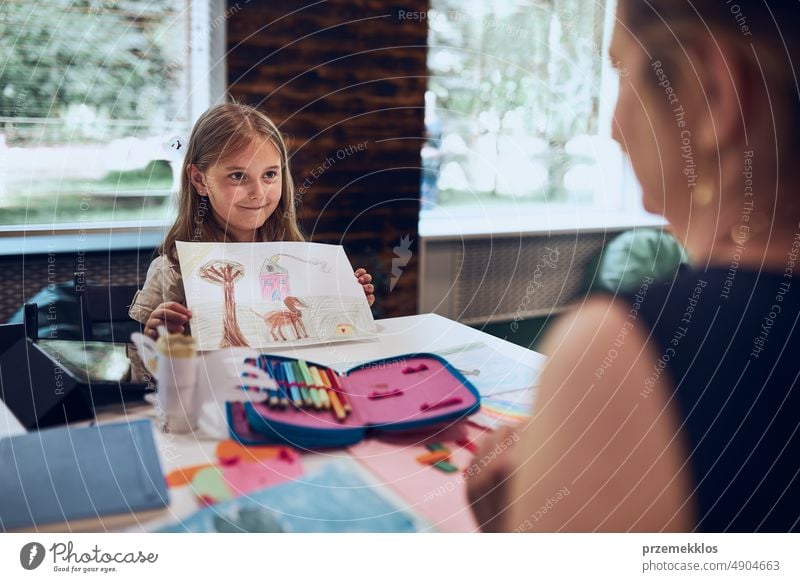 Girl presenting her artwork teacher. Woman assisting schoolgirl during classes at primary school. Child drawing picture sitting at desk in classroom. Learning at primary school. Back to school