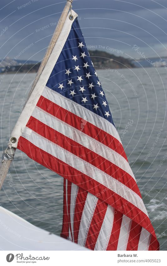 From the edge of a boat, the American flag with Alcatraz prison and the San fransisco bay in the background.. American Flag San Francisco Bay