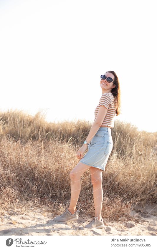 Happy young woman wearing sunglasses walking near the beach in dunes with tall dry grass. Photo in neutral beige colors. traveler beautiful landmark tourism