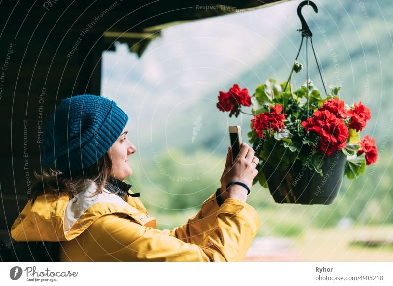 Young Woman Tourist Lady Photographs A Hanging Flower Pot On Phone beautiful beauty caucasian countryside decorate decoration decorative flower garden house