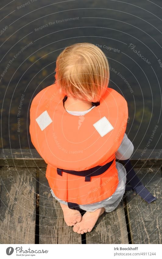 small child with life jacket squats on jetty and looks into water Child with life jacket Outdoors sunny wearing Ocean Summer youthful Water Life safety