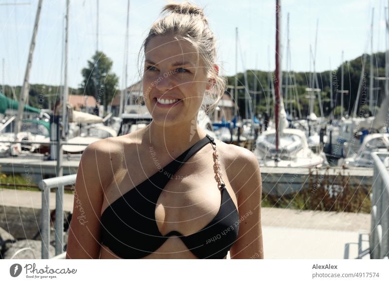 Young beautiful woman in black bikini on the pier of a sailboat harbor on the Baltic Sea Lifestyle Back-light salubriously pretty Woman Athletic Slim Esthetic