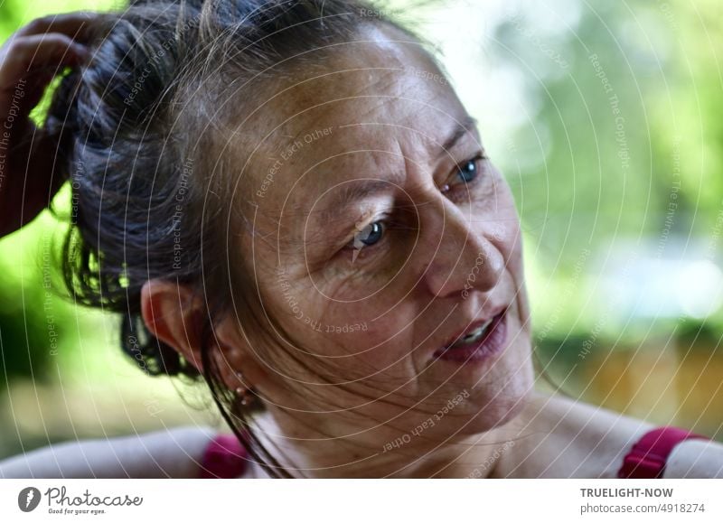 Woman. summer expressive in half profile looking into distance, bare shoulders with red straps and still wet hair on shore after swimming in river Face