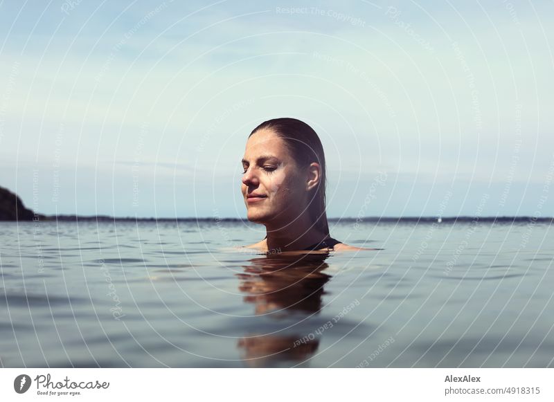 Young beautiful woman in the shallow water in the Baltic Sea smiles contentedly with closed eyes Lifestyle Back-light salubriously pretty Woman Athletic Slim