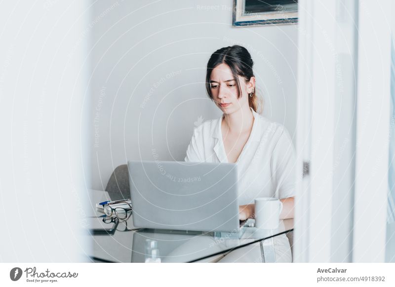 Creative young woman working on laptop in her studio remotely while looking concentrated. Typing and searching on the laptop using internet. Looking for new job freelance. Home office concept.