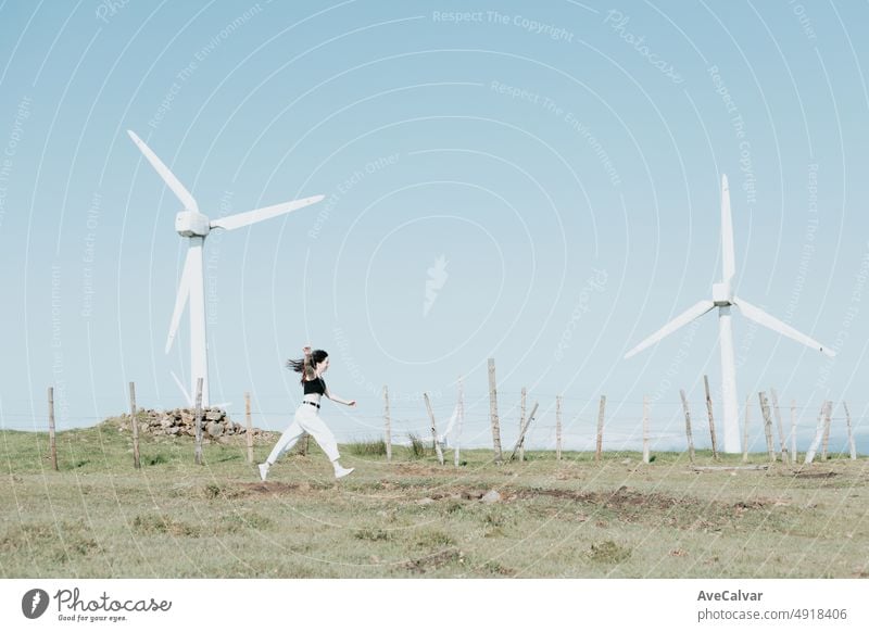 Gen Z girl running surrounded by eolic electric energy powered windmills, new power resources concept.Save the planet, side shot with copy space for text carefree happy fun motion