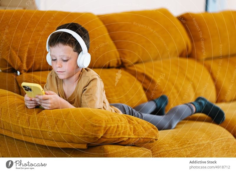 Boy lying on a sofa using the mobile phone child boy home technology smartphone kid headphones young listen serious concentrated movie lifestyle
