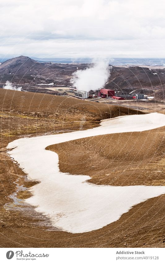 Arid volcanic terrain against cloudy sky on winter day hill valley landscape nature countryside steam snow mountain scenic field grass environment geyser slope