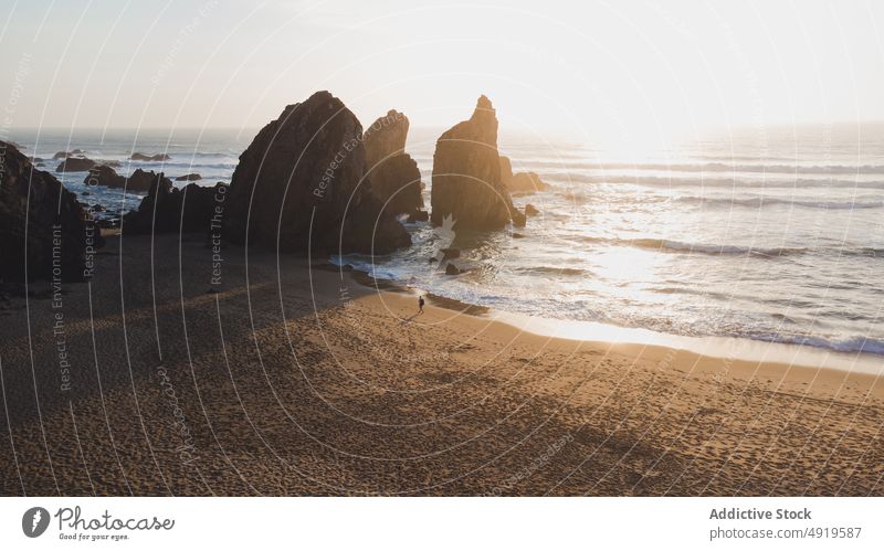 Shore near sea with cliffs at sunset time person walk rock beach water shore nature coast island tropical evening sundown summertime sunlight sand resort