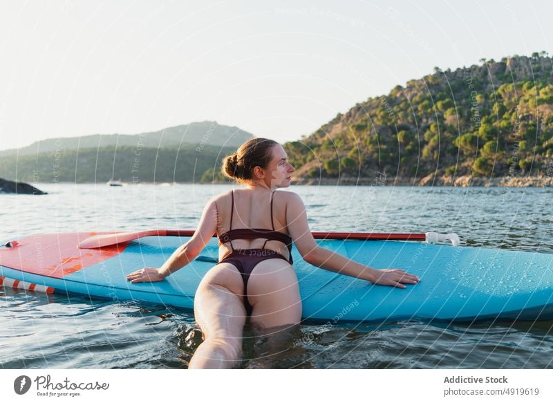 Woman lying on paddleboard in lake woman leisure hobby water rest nature wellbeing swimwear summer sup board slender shore float relax forest vacation coast