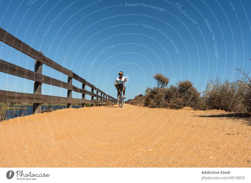 Black woman riding a bike on a terrain path female black bicycle catwalk girl young summer spring walkway summertime sunglasses healthy town ride outdoor nature