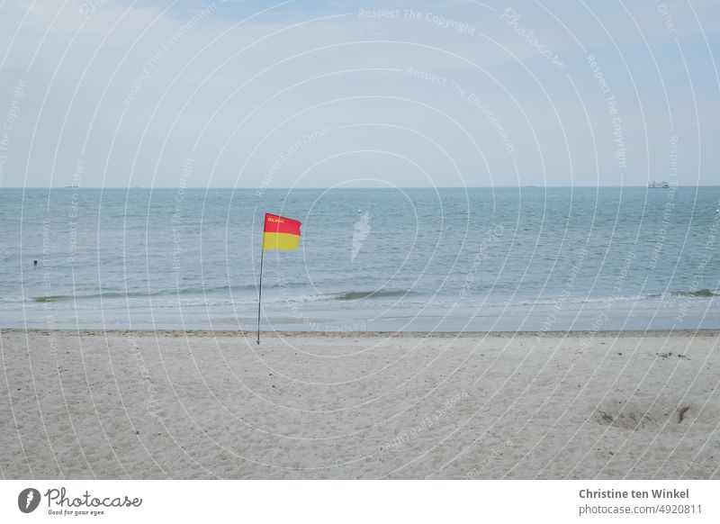 A DLRG flag flies in the cloudy weather on the empty North Sea beach, the head of a swimmer can be seen in the water. dlg Water rescue organization