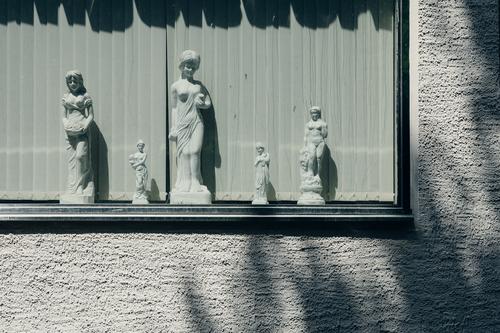 Female statues made of plaster in a window in front of slats, rough plastered wall and shadow Statue feminine Gypsum Window Sun Wall (building) Plaster harsh