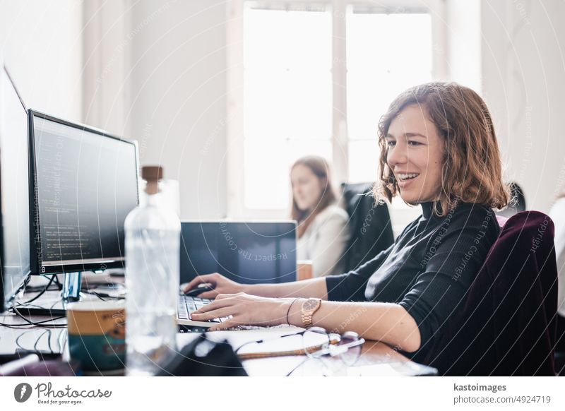 Women in startup business and entrepreneurship. Yound devoted female AI programmers and IT software developers team programming on desktop computer in startup company share office space.